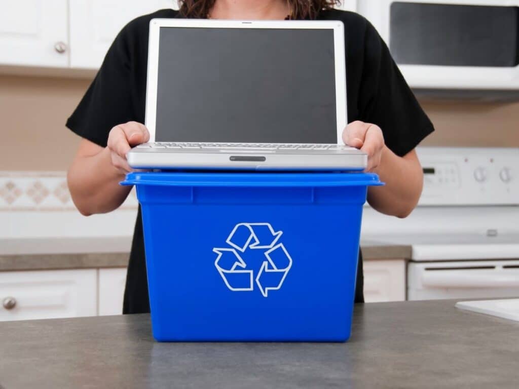 Individual dropping laptop into blue recycling bin